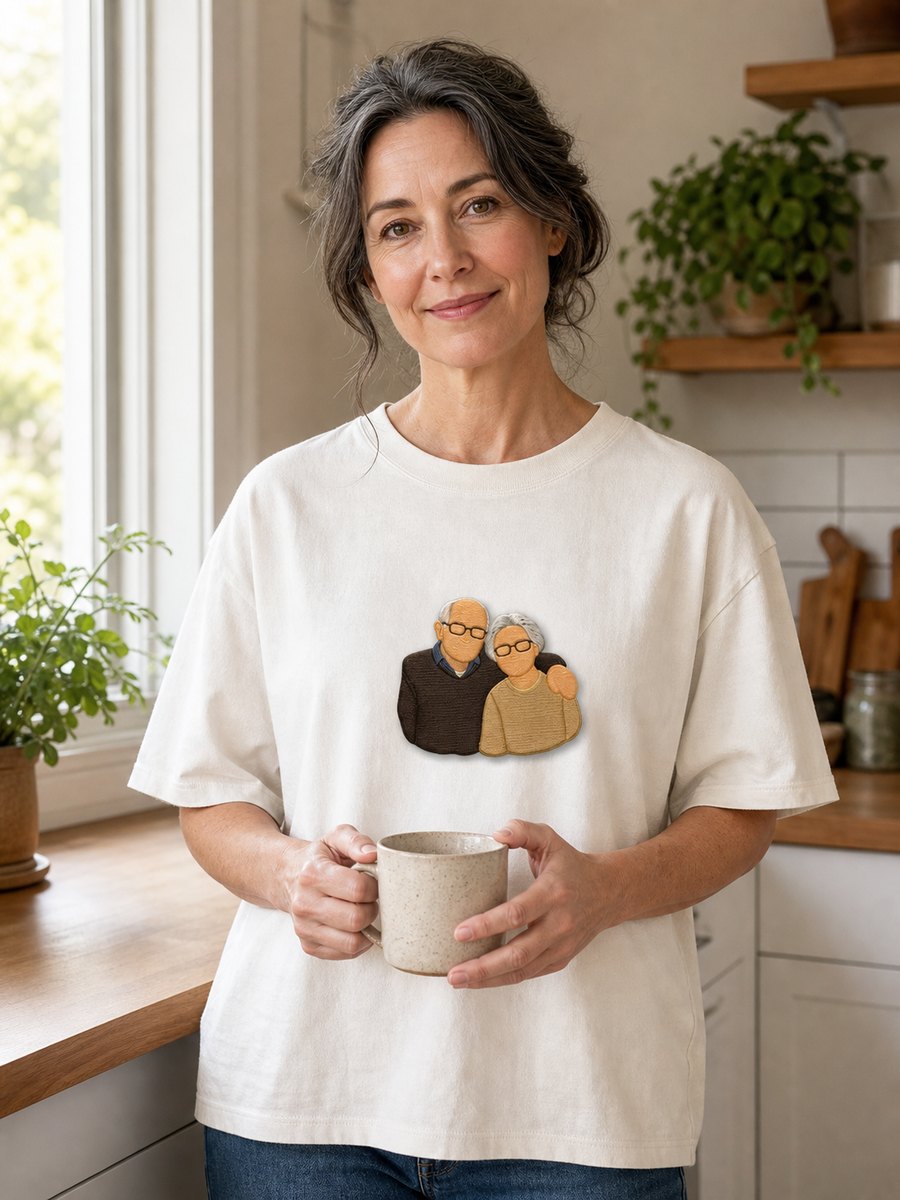 A woman in a bright kitchen wearing a tee with her parents embroidered on the chest
