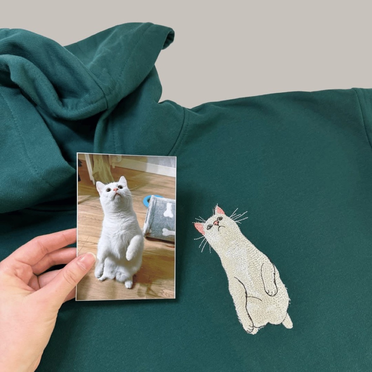 A white cat embroidered on a natural tee, photographed in the shop